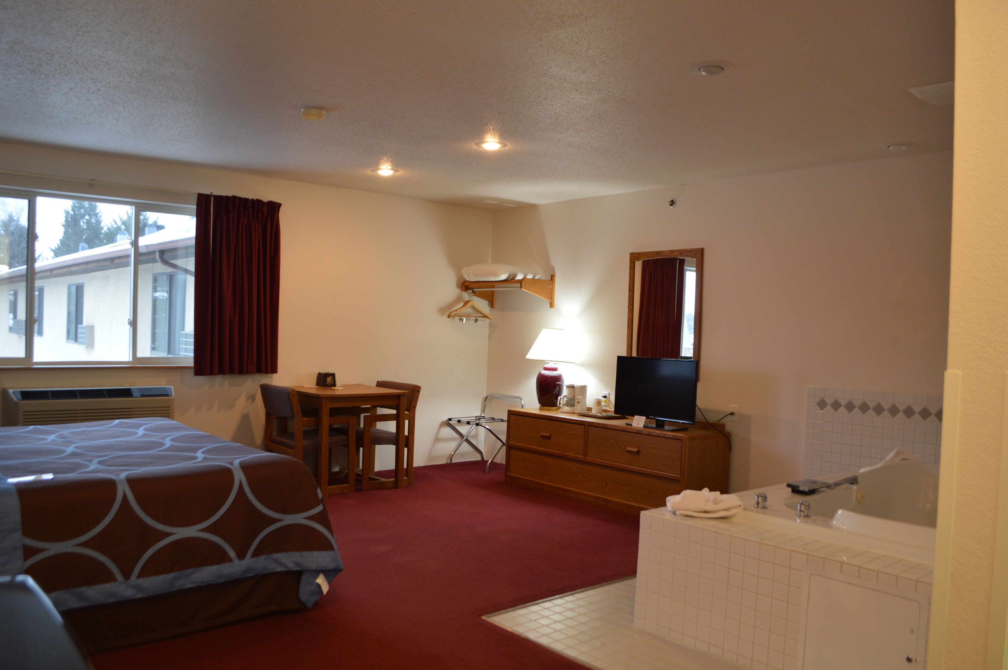 A hotel room with a bed, a desk, a chair, a TV, a lamp, a dresser, and a bathroom with a bathtub and sink.