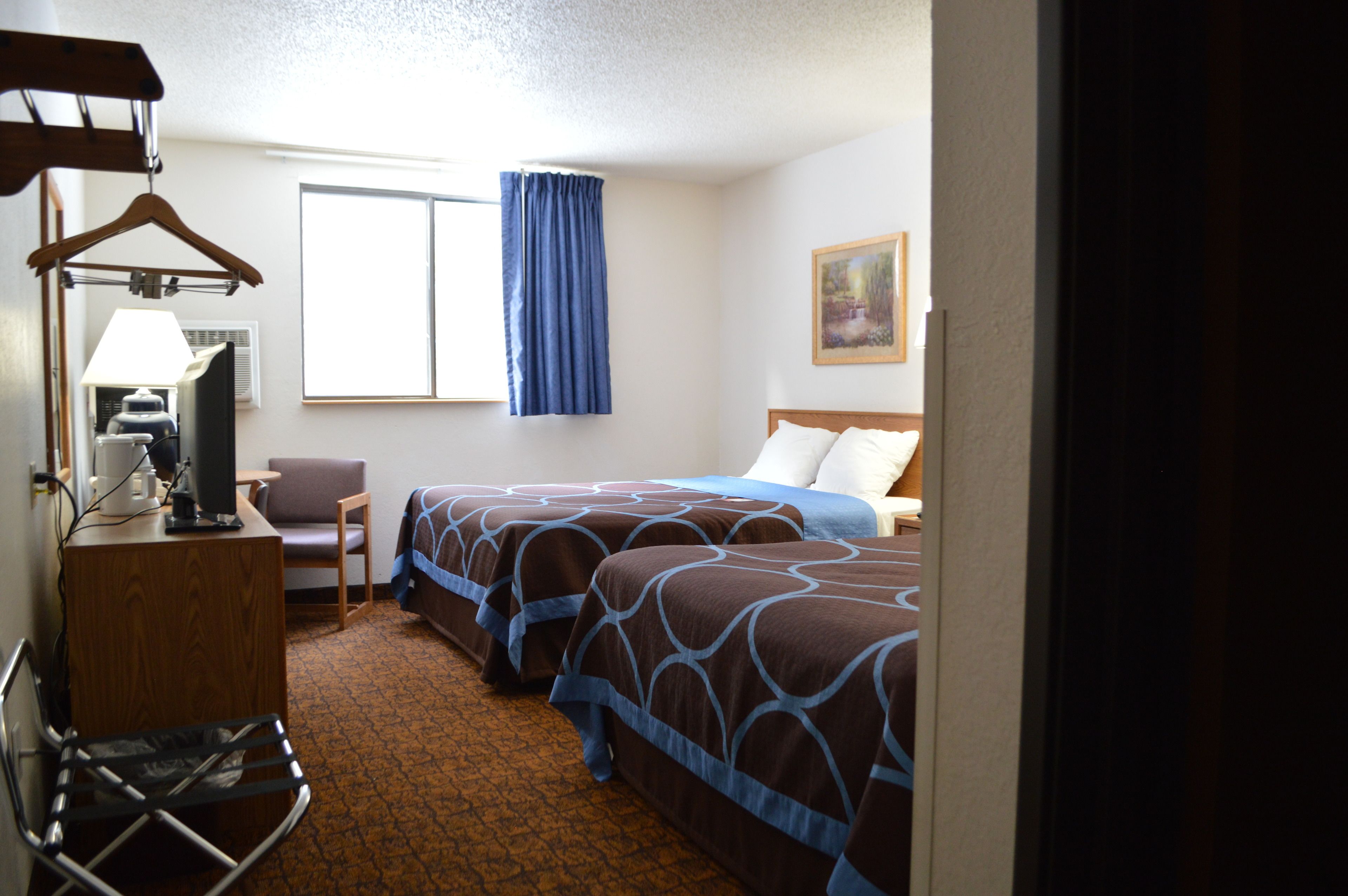 A hotel room with two beds, a desk with a lamp, a chair, and a window with curtains.