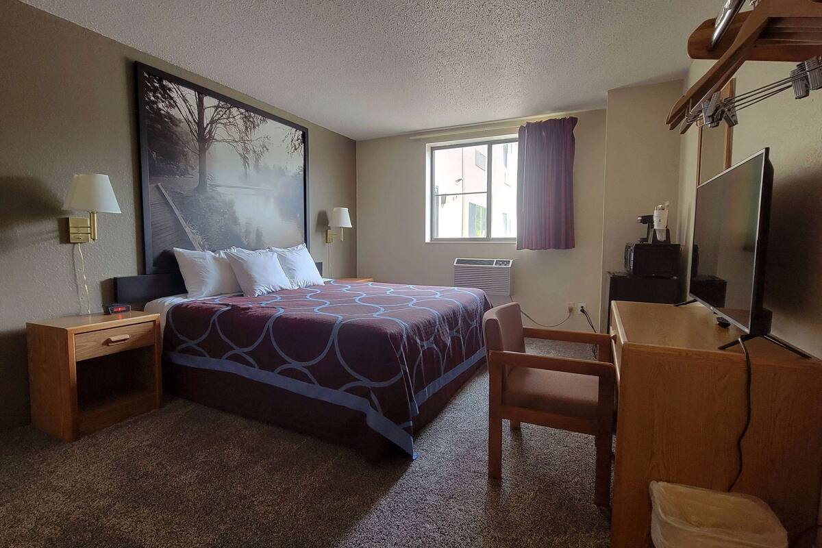 Une chambre d’hôtel équipée d’un lit, d’un bureau, d’une chaise, d’une télévision et d’une fenêtre avec des rideaux.