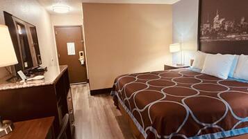A hotel room with a bed, a desk with a telephone, a mirror, and a wall-mounted picture.