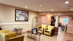 Un hall d’hôtel avec des fauteuils jaunes, un comptoir d’accueil, un panneau d’accueil encadré et un espace restaurant bien visible.