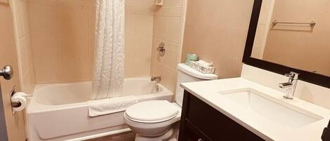 Une salle de bain équipée d’une baignoire, de toilettes et d’un lavabo, avec un plancher en bois et des murs de couleur beige.