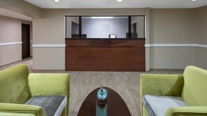 Un espace d’accueil comprenant un bureau en bois, deux fauteuils verts et une petite table ornée d’un objet décoratif.