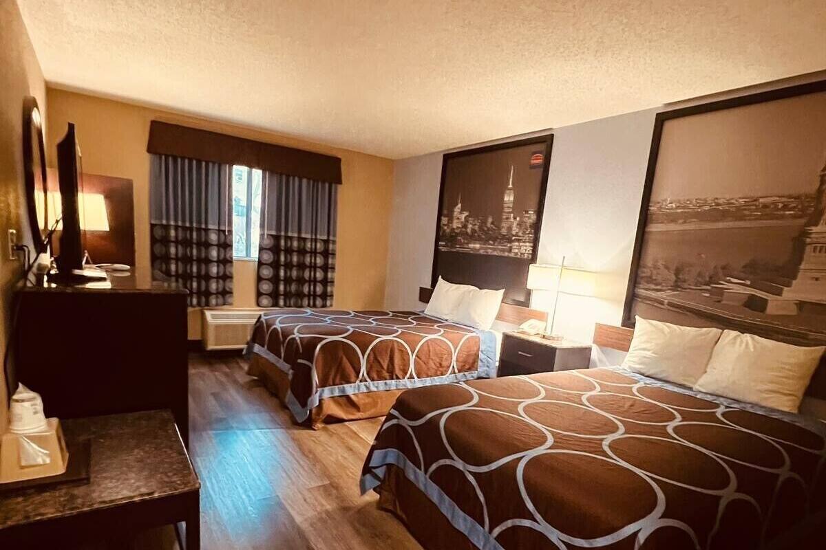 A hotel room with two beds, a desk, a chair, and a large window with curtains.