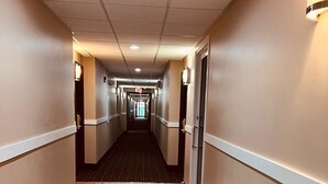 Un couloir d’hôtel avec un plancher en bois, des murs de couleur beige et un plafond doté d’un éclairage encastré.