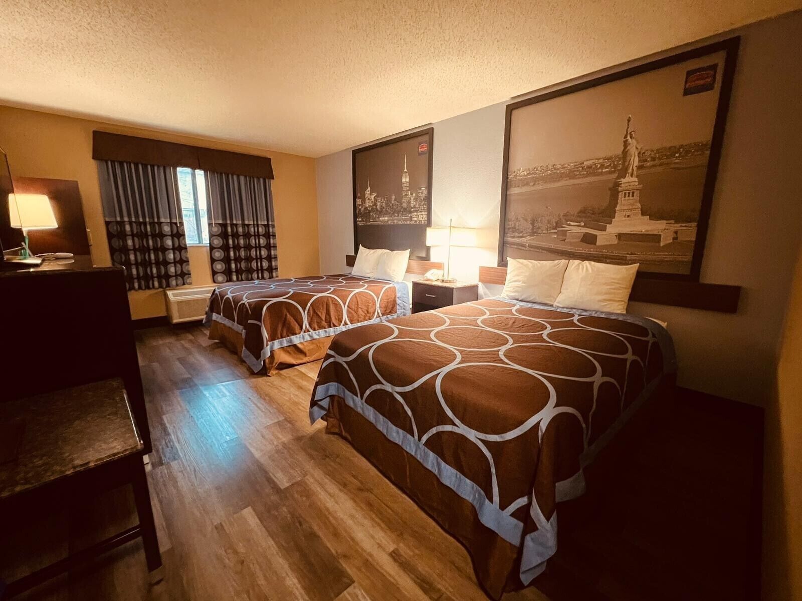 Ett hotellrum med två sängar, ett skrivbord, en stol och ett fönster med gardiner.