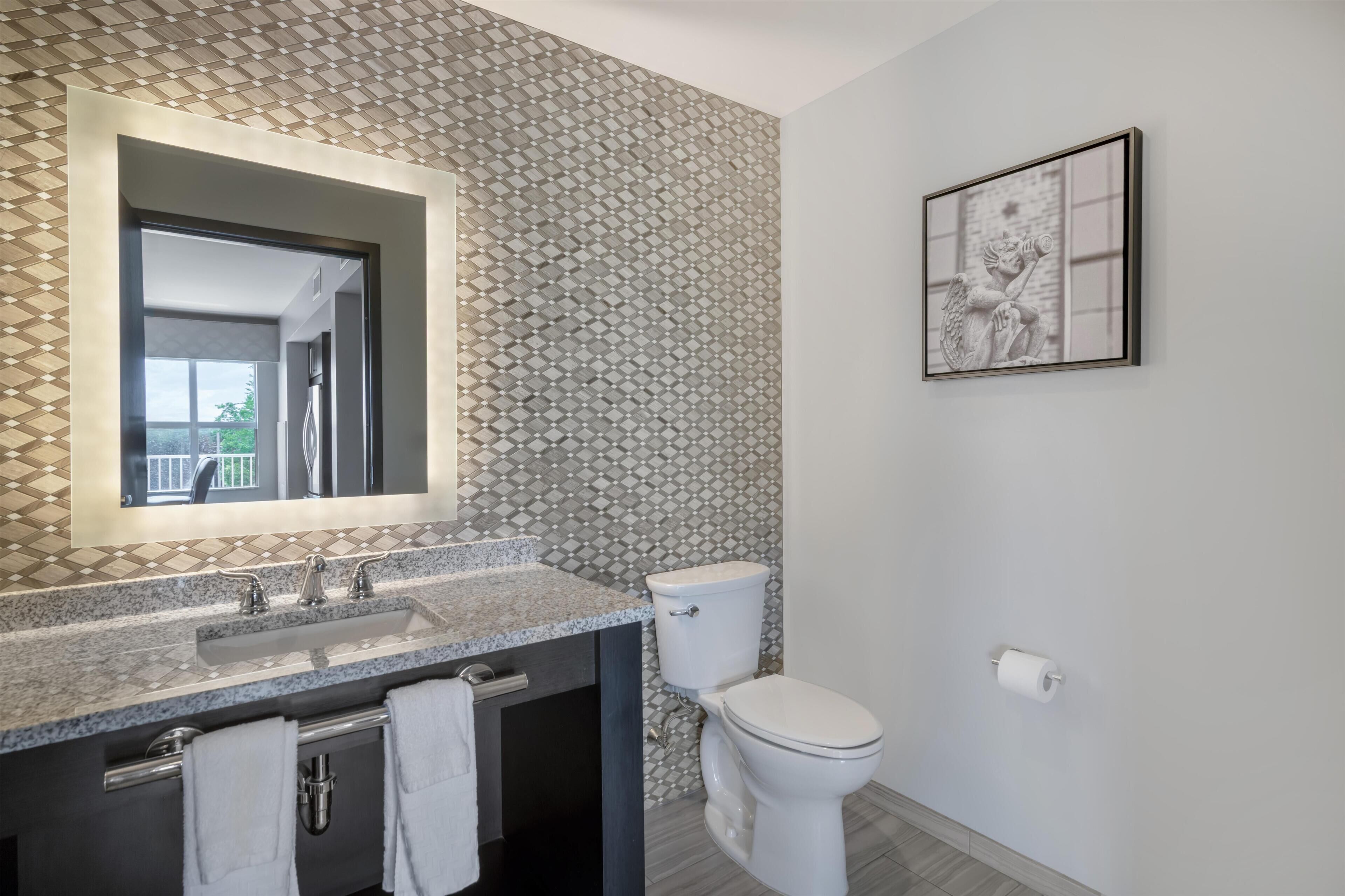 Une salle de bain avec un comptoir en granit, des toilettes blanches et un mur à motifs.