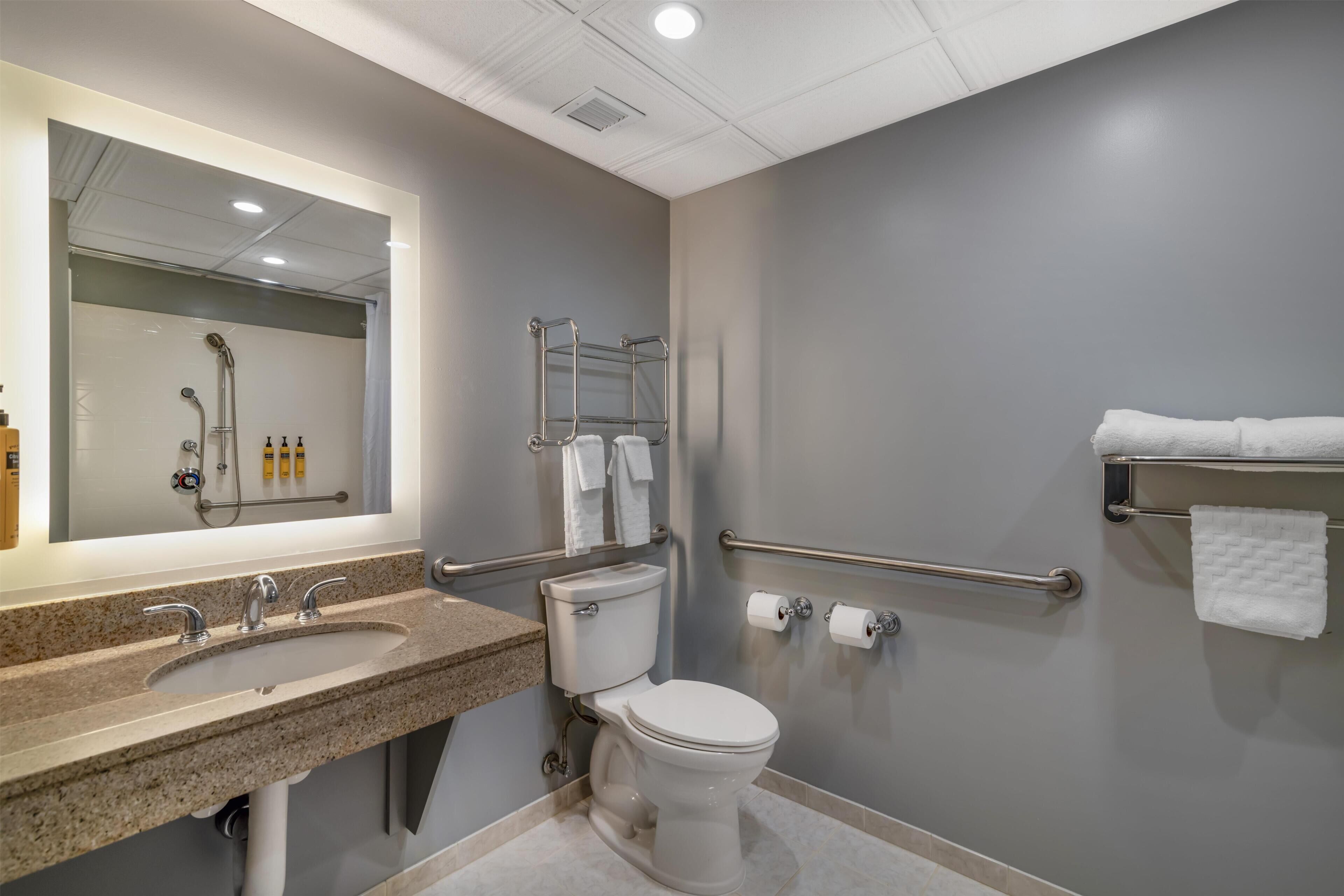 Un baño moderno con encimera de granito, inodoro blanco, secamanos y toallero.