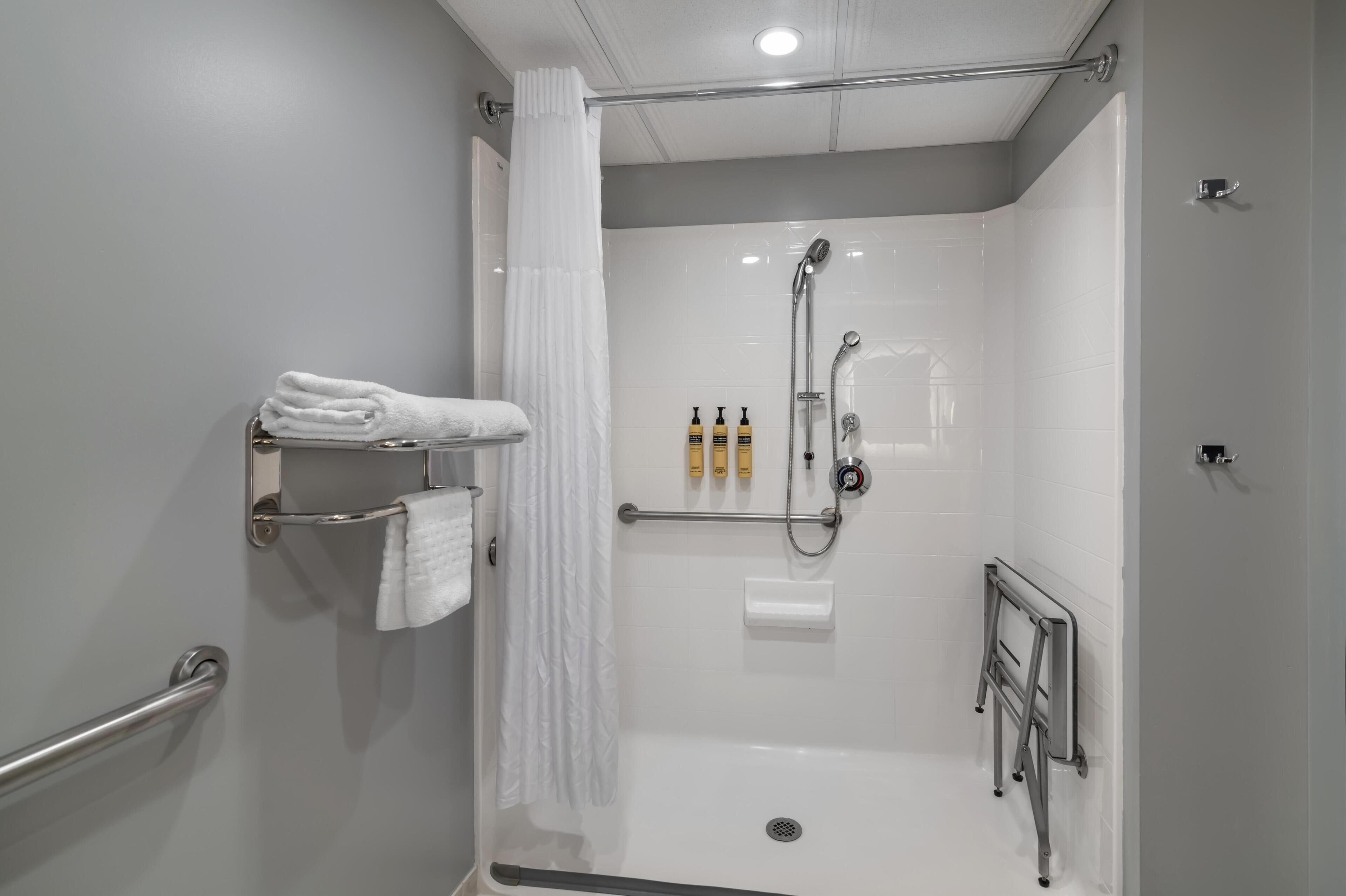 Une salle de douche moderne dotée d’une porte en verre, d’une barre d’appui, d’un porte-serviettes et d’un ensemble de produits de toilette.