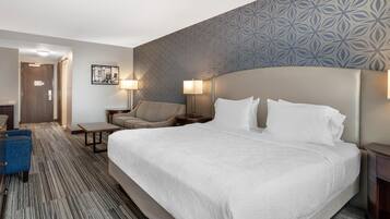 Une chambre d’hôtel avec un grand lit, deux tables de chevet, une chaise, un bureau et un mur décoré d’un motif.
