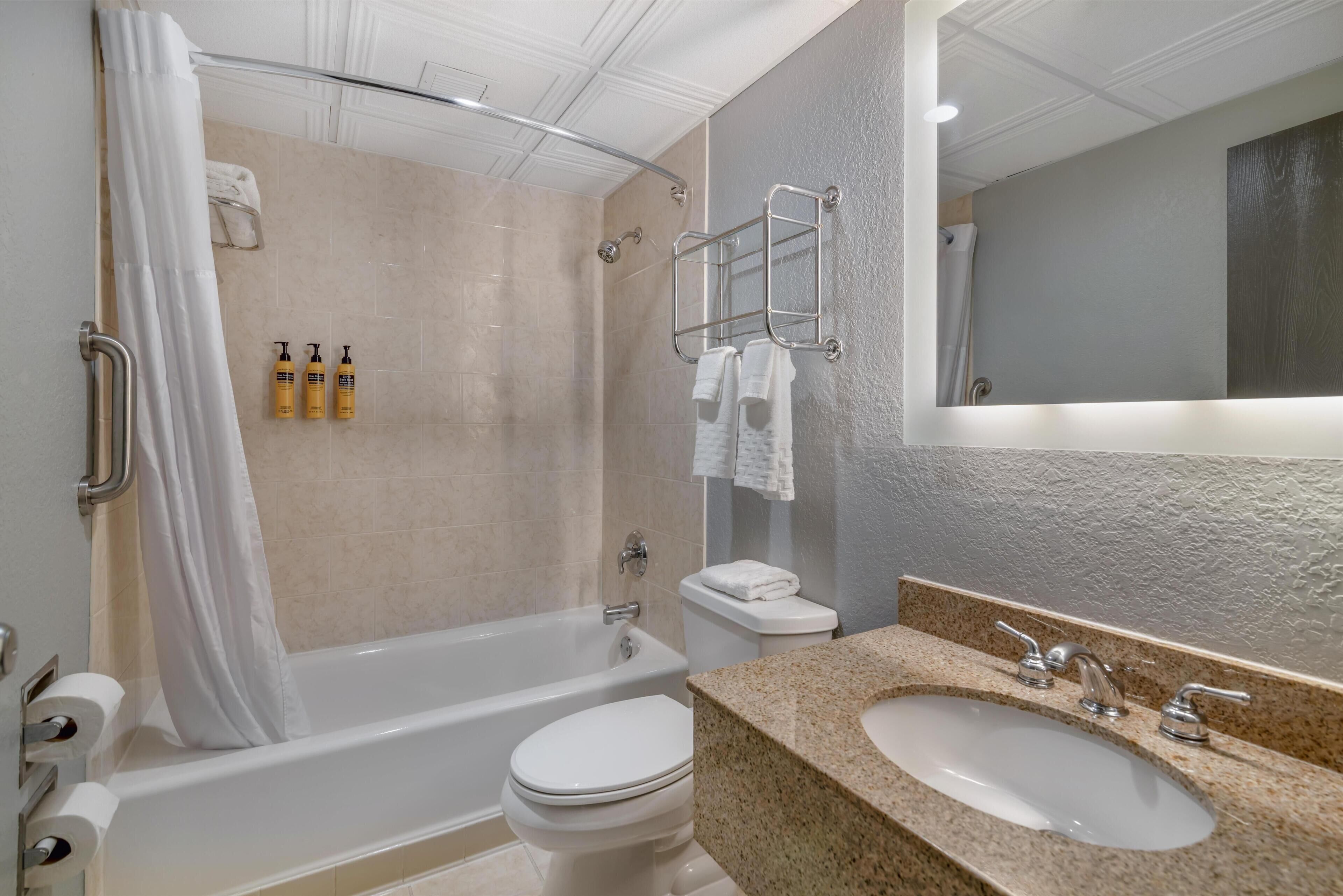 A modern bathroom with a bathtub, toilet, and sink, featuring a shower curtain, towel rack, and toiletries.
