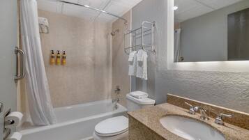 A modern bathroom with a bathtub, toilet, and sink, featuring a shower curtain, towel rack, and toiletries.