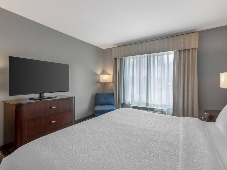 A hotel room with a large bed, a flat-screen TV, a desk, a chair, and a window with curtains.