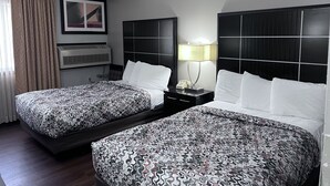 A hotel room with two beds, a nightstand with a lamp, a framed picture on the wall, and an air conditioning unit.