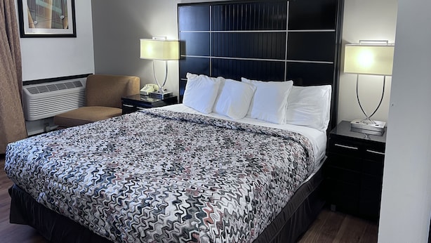 A hotel room with a large bed, two bedside tables, a chair, a wall-mounted air conditioner, and a framed picture. - AmeriVu Inn (Park Falls)
