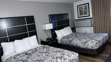 A hotel room with two beds, a bedside table with a lamp, a phone, and a wall-mounted air conditioning unit.