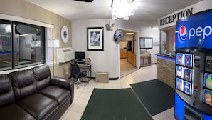 A reception area with a couch, a Pepsi vending machine, and a window with a view of a bar. - AmeriVu Inn (Park Falls)