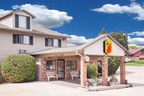 A motel with a 'Super 8' sign, a 'Low Clearance' sign, and a covered parking area with two white chairs.