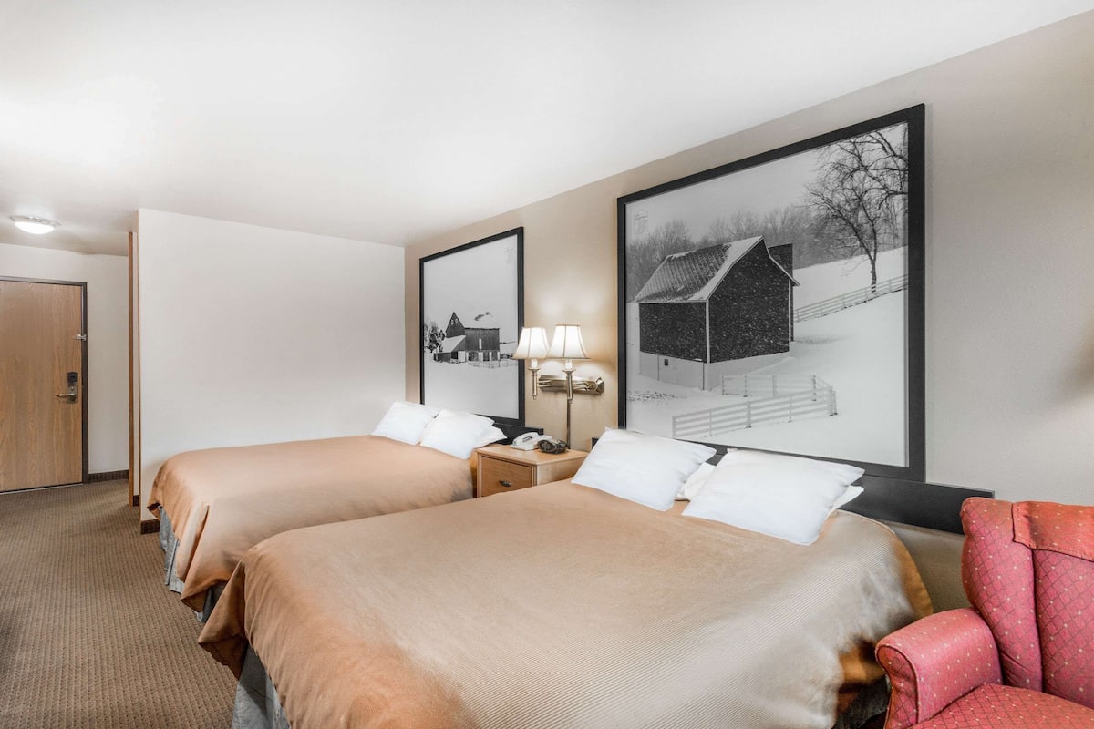 Une chambre d’hôtel avec deux lits, une table de chevet avec une lampe et une chaise rouge.