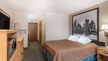 A hotel room with a bed, a television, a wooden dresser, and a framed picture on the wall.