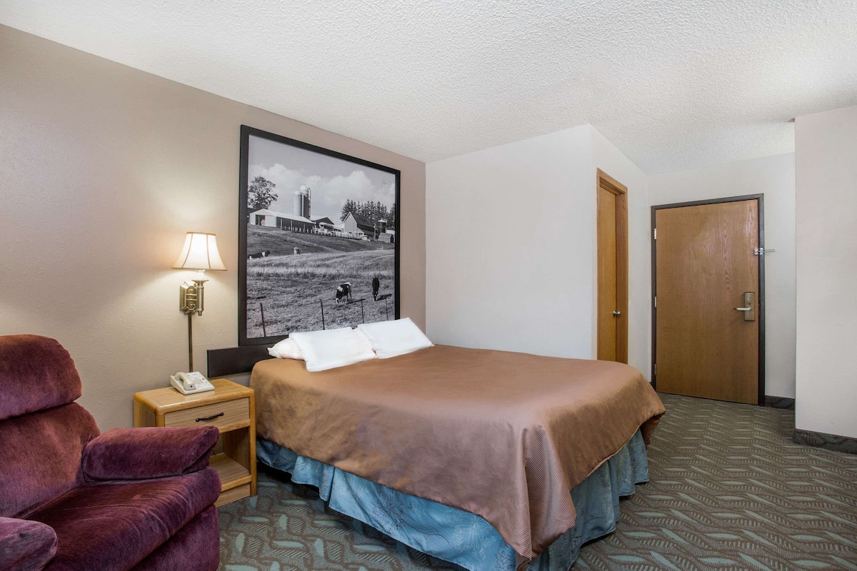 Une chambre d’hôtel avec un lit, une table de chevet avec une lampe, une chaise et une porte.