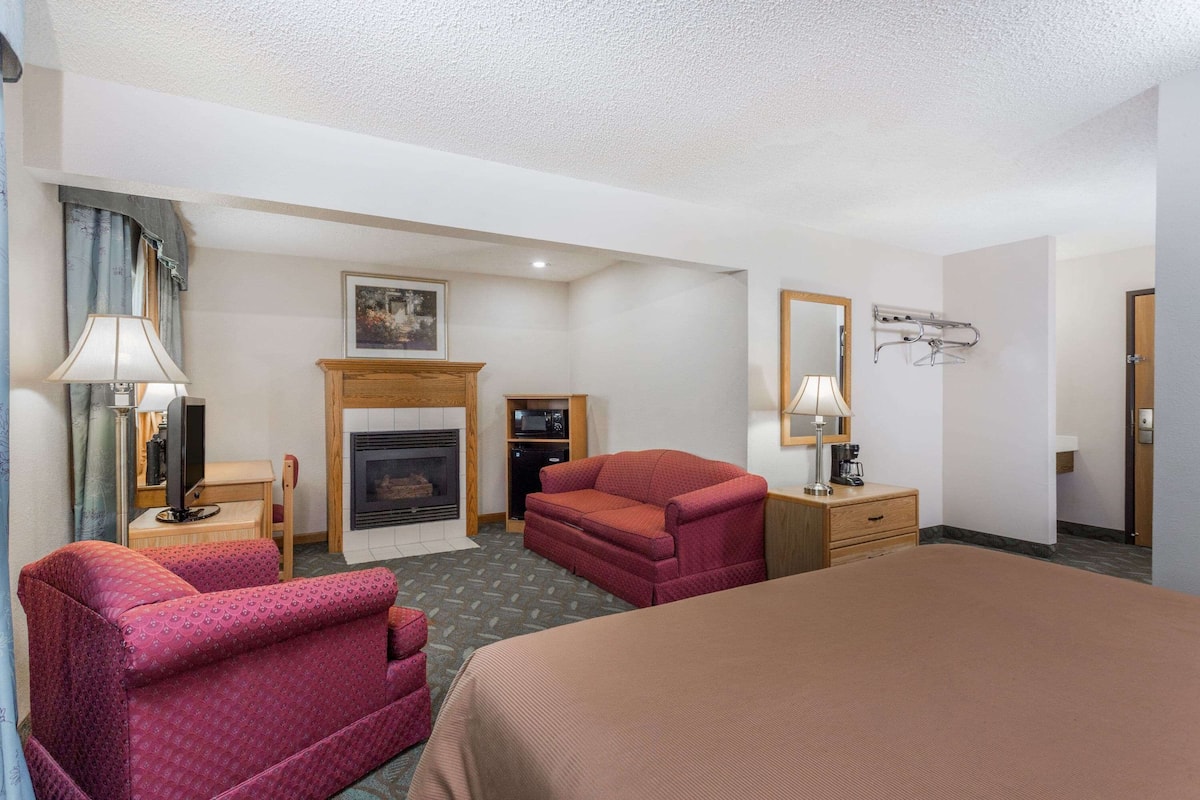 Une chambre d’hôtel comprenant un lit, deux fauteuils, un canapé, une cheminée, une télévision et un porte-manteau.
