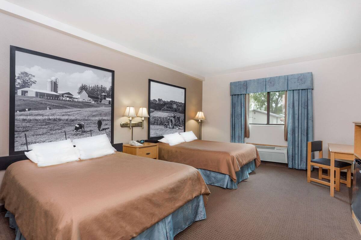Une chambre d’hôtel avec deux lits, un bureau, une chaise et une grande fenêtre avec des rideaux.