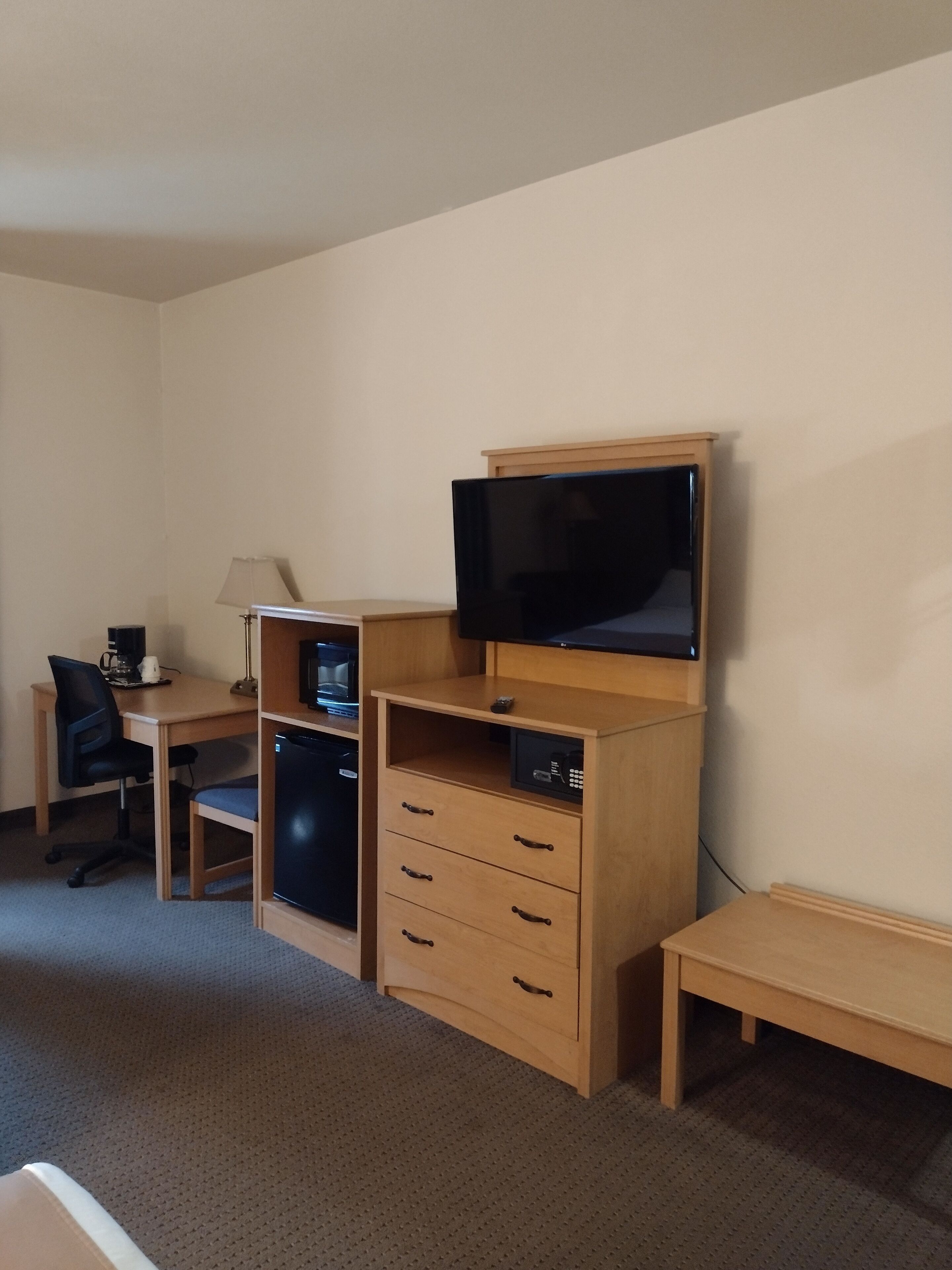 Ein Hotelzimmer mit einem Holztisch, einem Fernseher darauf, einem kleinen Kühlschrank, einer Lampe und einem Stuhl.