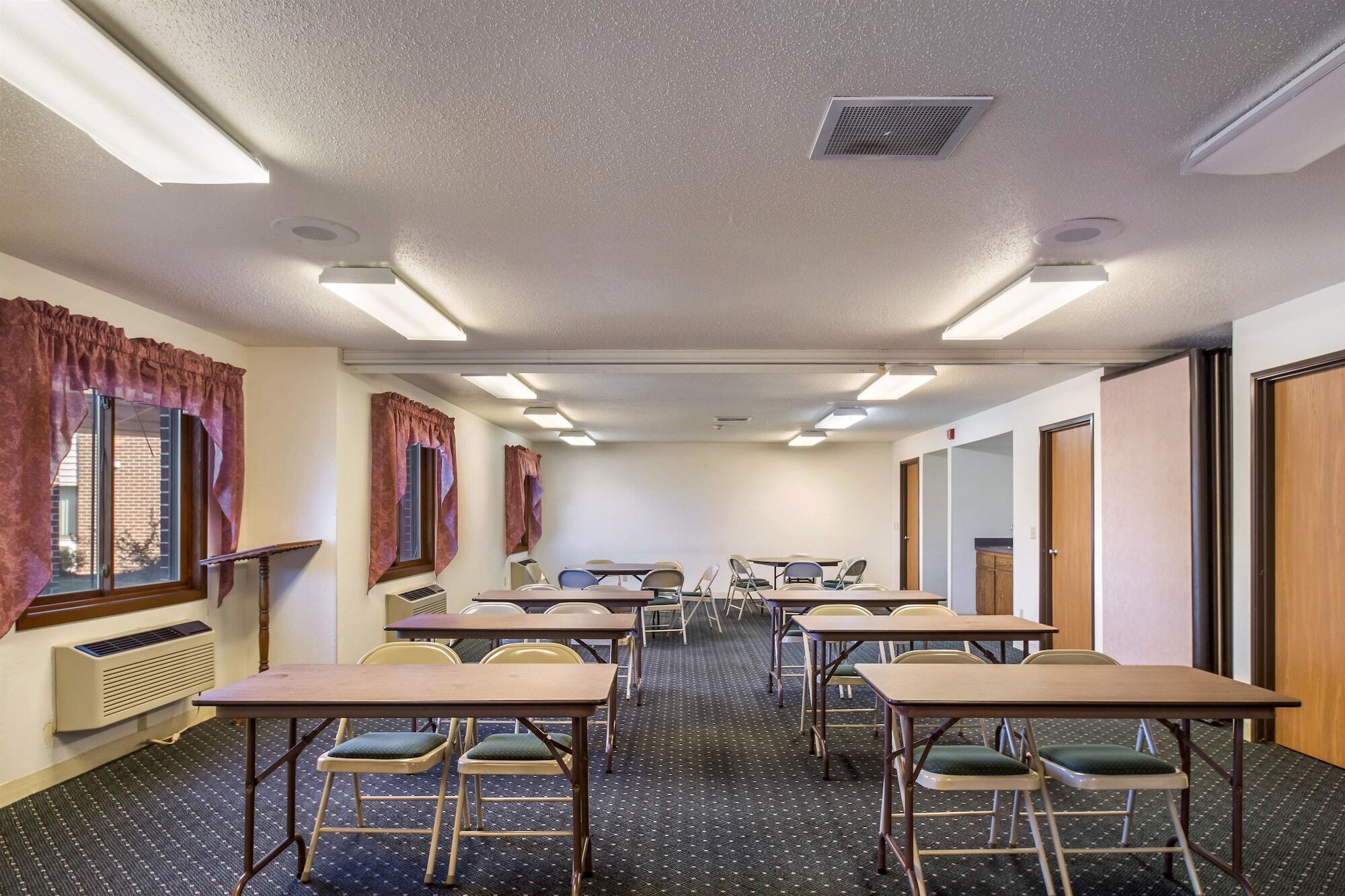 A conference room with tables and chairs, a projector screen, and a window with curtains.