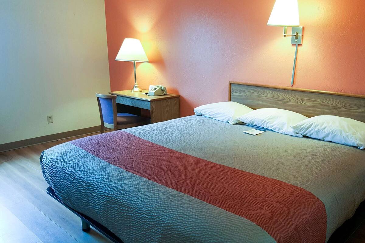 A hotel room with a bed, a desk, two bedside lamps, and a telephone.
