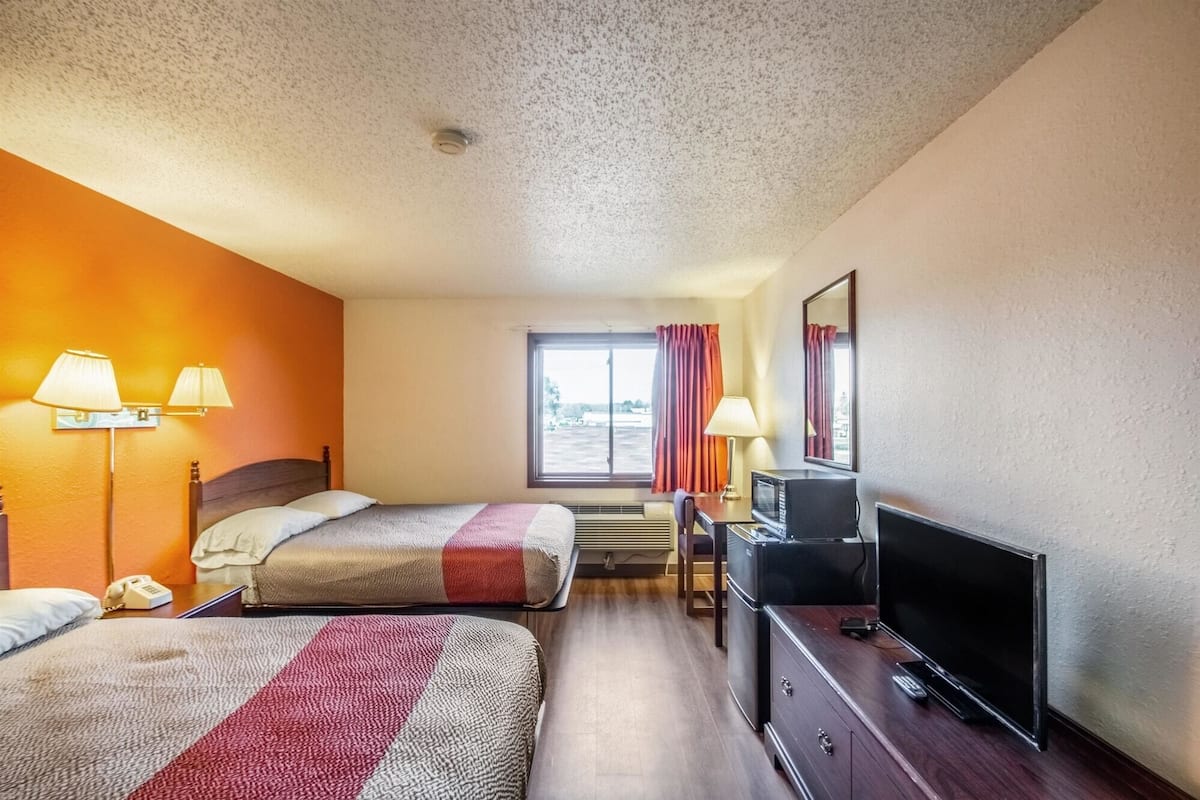 A hotel room with two beds, a desk with a TV, a telephone, and a window with curtains.