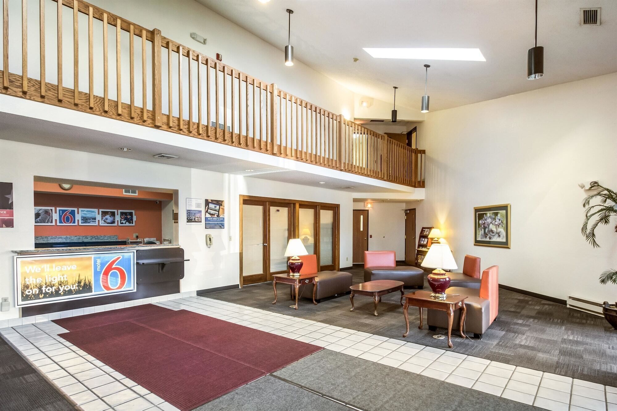 A hotel lobby with a reception desk, seating area, and a wooden balcony.