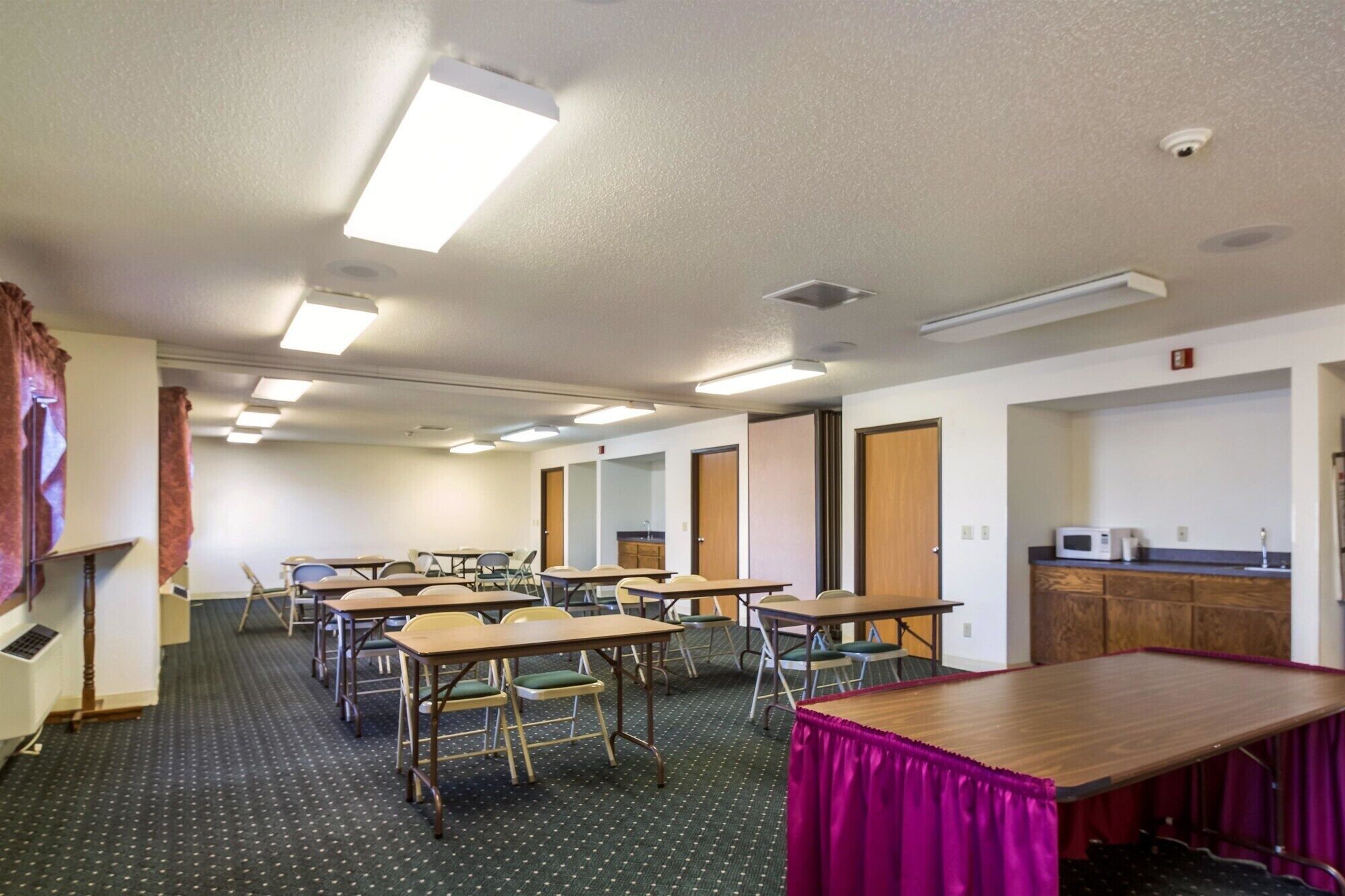 Une salle de conférence équipée de plusieurs tables et chaises, d’un coin cuisine et d’une porte donnant sur une autre pièce.