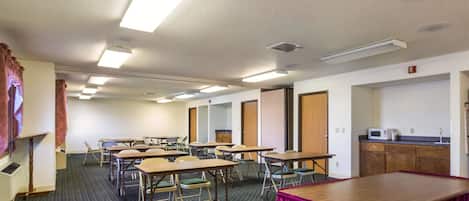 Une salle de conférence équipée de plusieurs tables et chaises, d’un coin cuisine et d’une porte donnant sur une autre pièce.