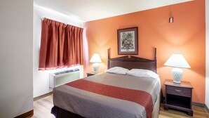 A hotel room with a bed, two bedside lamps, a window with curtains, a wall-mounted picture, and a radiator.
