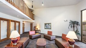 A spacious lobby with a high ceiling, a wooden staircase, and a seating area with cushioned sofas and tables.