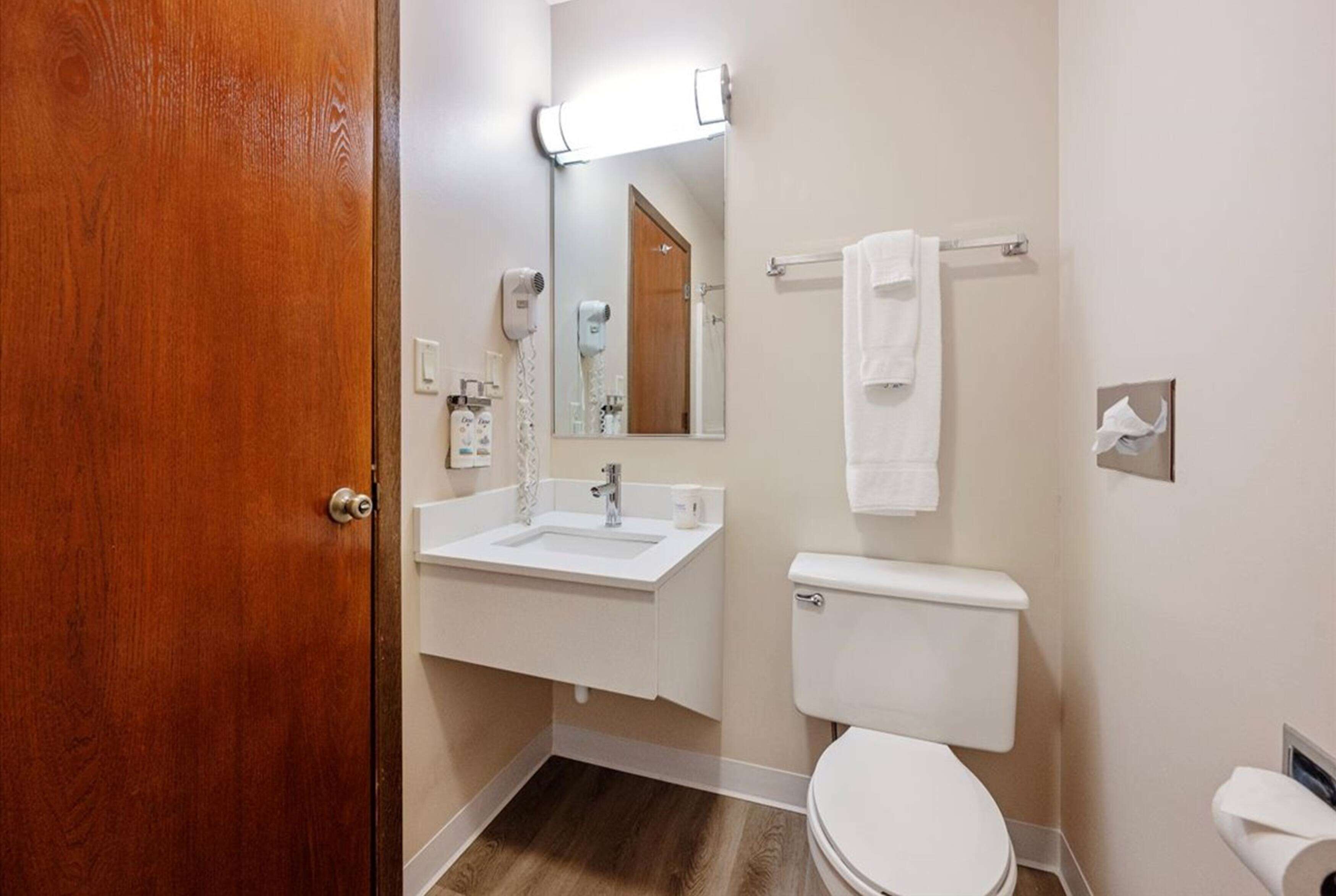 Un baño con puerta de madera, lavamanos blanco y retrete.
