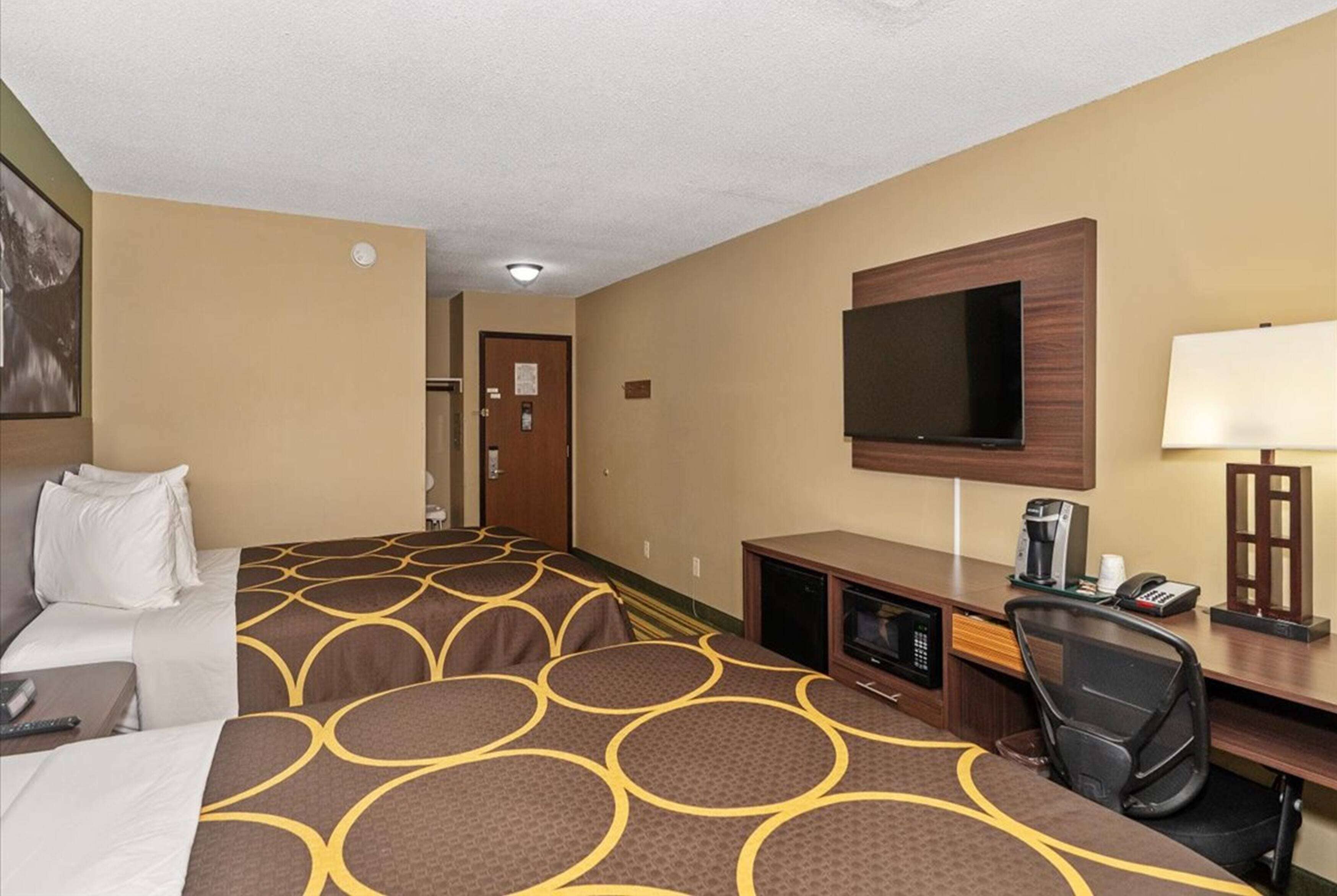 Habitación de hotel con dos camas, un televisor, un escritorio con ordenador y cafetera.