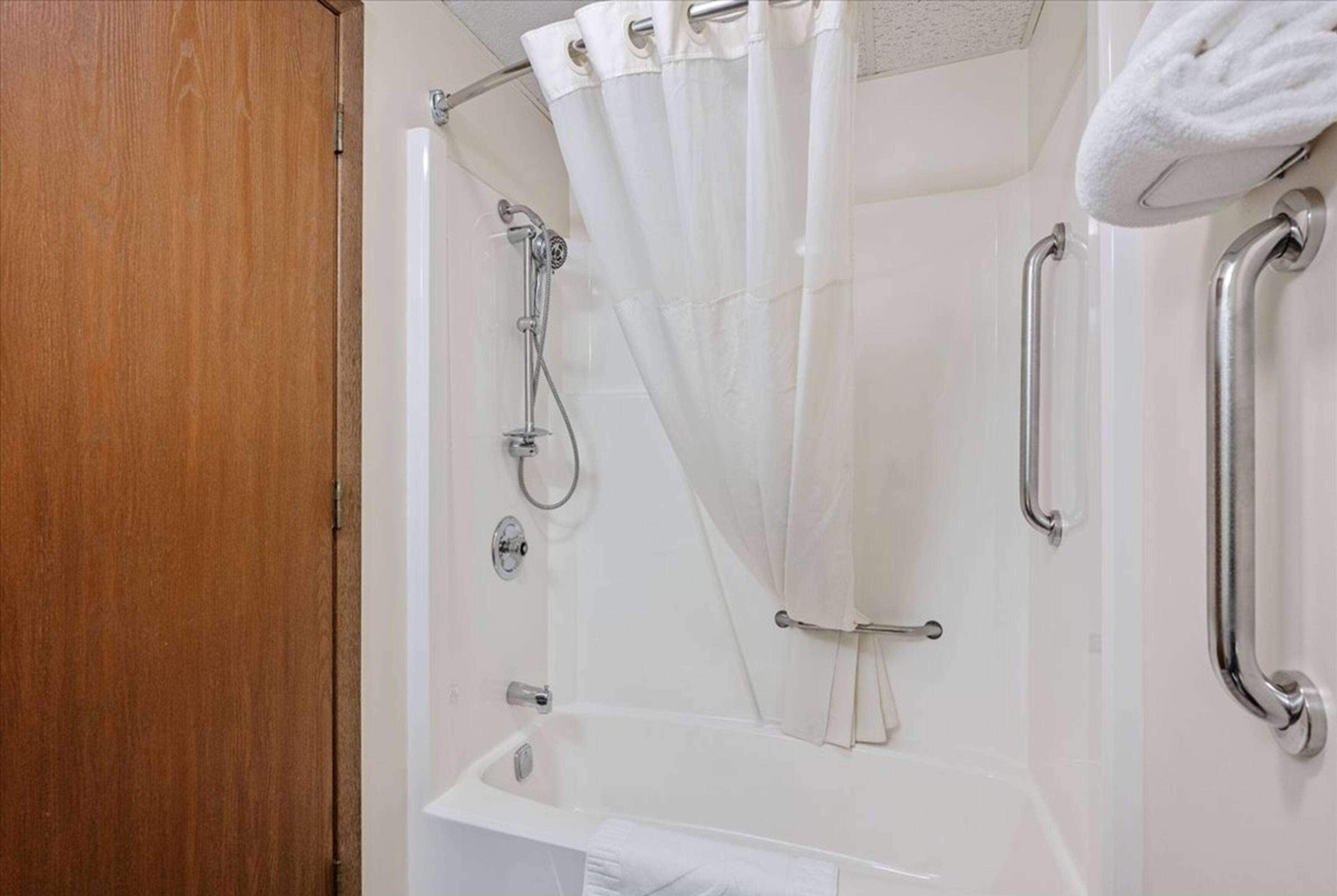 A shower with a glass door, a handheld showerhead, and a white curtain.