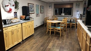 Una cocina con armarios de madera, una zona de comedor con sillas, un refrigerador y una ventana con persianas.