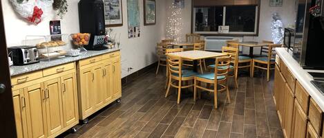 Una cocina con armarios de madera, una zona de comedor con sillas, un refrigerador y una ventana con persianas.