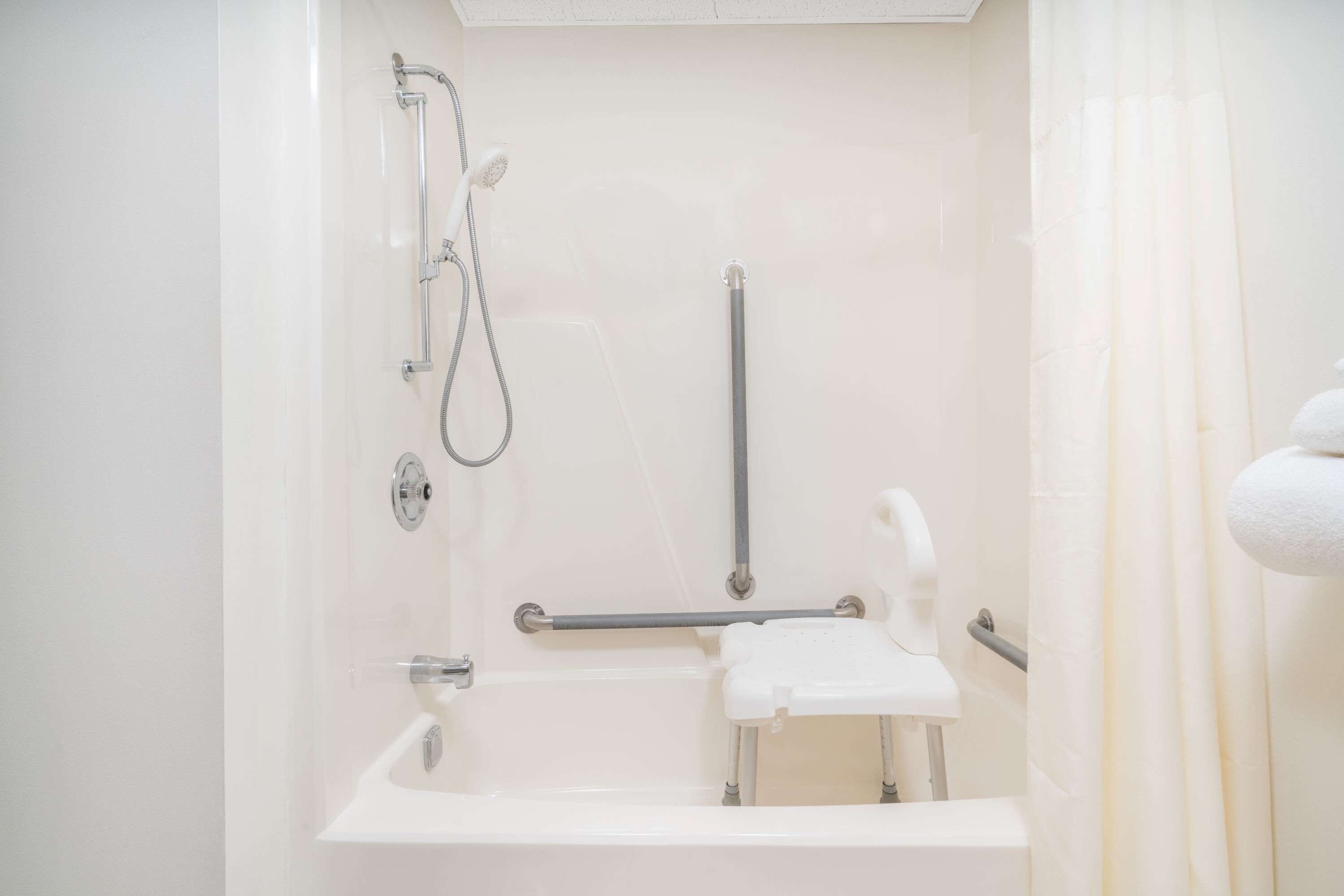 Ein Badezimmer mit einer weißen Badewanne, Haltegriffen, einer Duschbrause und einem Handtuchhalter.