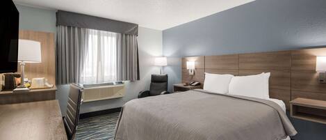 A hotel room with a large bed, a desk, a chair, a TV, and a window with curtains.