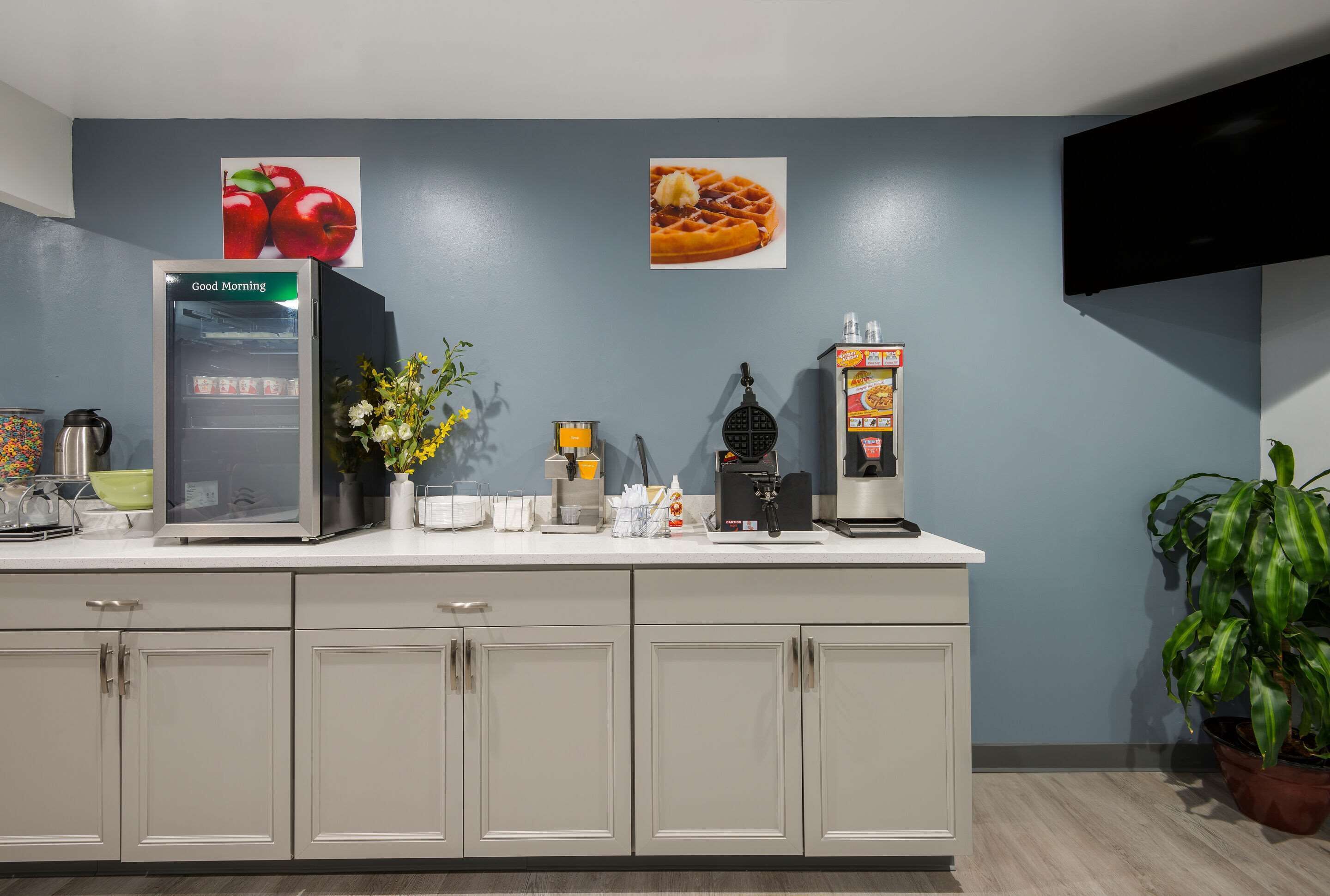 A modern kitchen with a refrigerator, coffee machine, waffle maker, and a potted plant.