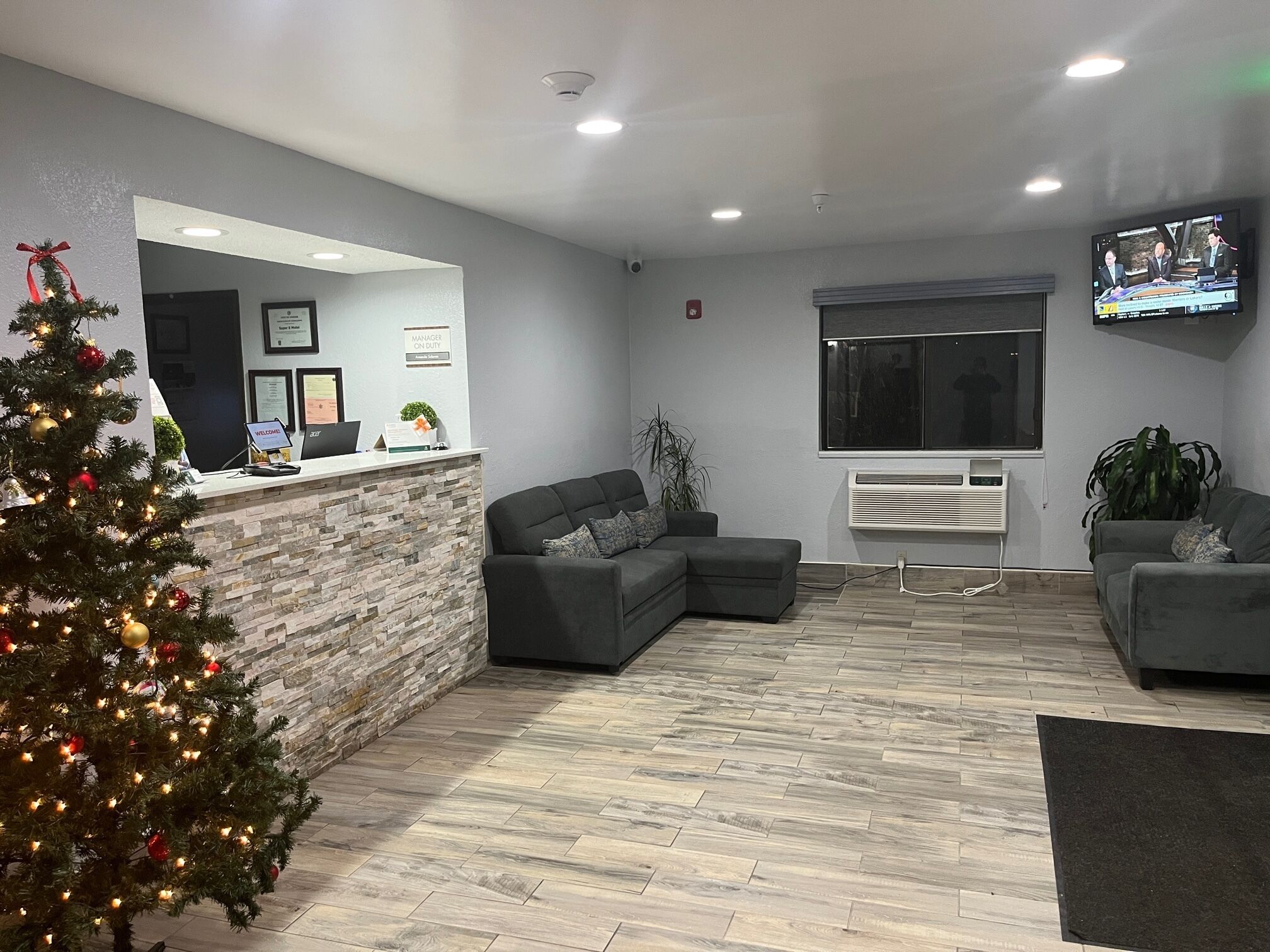 A modern reception area with a stone counter, grey sofas, a Christmas tree, and a flat-screen TV on the wall.