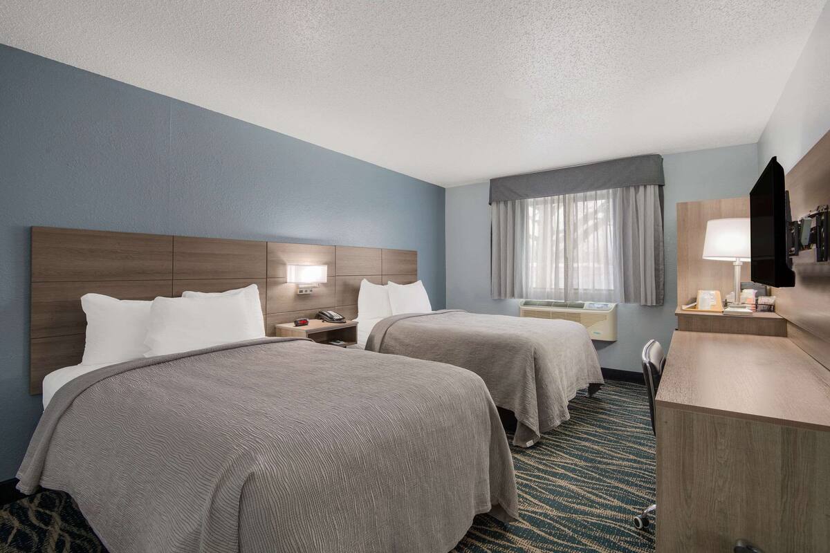 A hotel room with two beds, a desk, a chair, a TV, and a window with curtains.