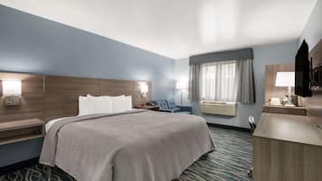 A hotel room with a large bed, bedside tables, a desk, a chair, a TV, and a window with curtains.