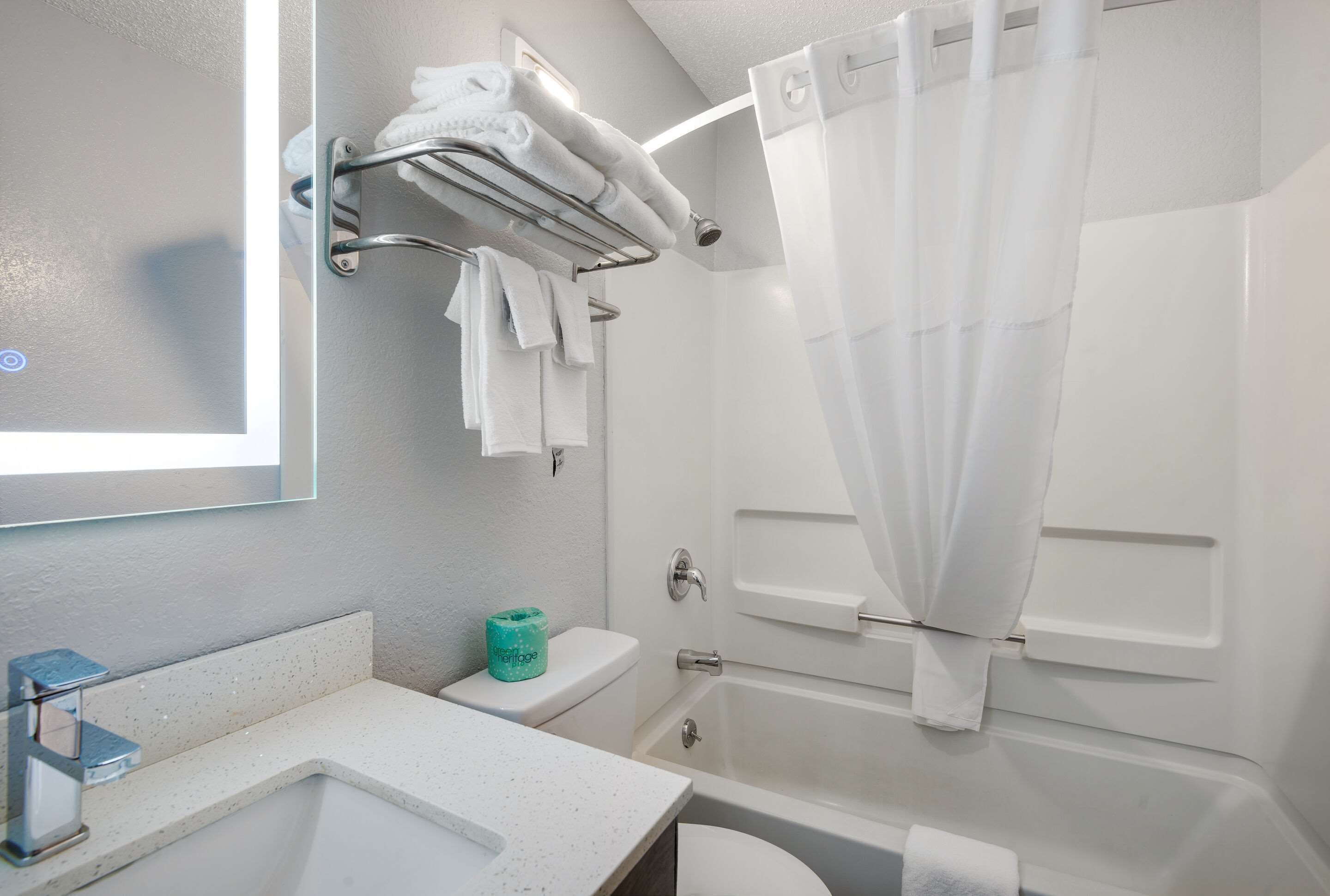 A bathroom with a white sink, toilet, and bathtub. There is a towel rack with folded towels and a shower curtain.