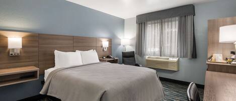 Une chambre d’hôtel avec un grand lit, des tables de chevet, un bureau, une chaise, une lampe de bureau, une fenêtre avec des rideaux et un climatiseur fixé au mur.
