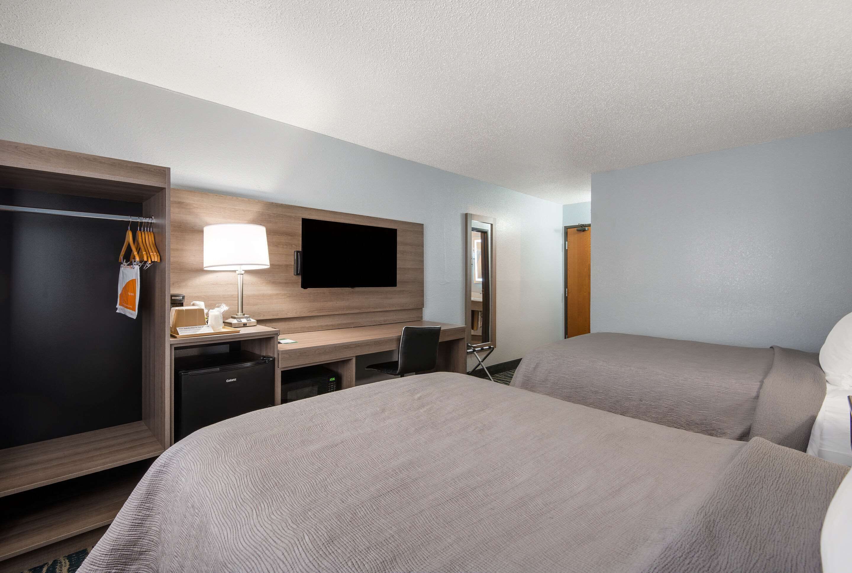 Une chambre d’h ôtel avec deux lits, un bureau avec une lampe, une télévision, une armoire et un miroir.